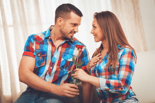 Handsome young man in love give red rose to his girlfriend in an apartment.