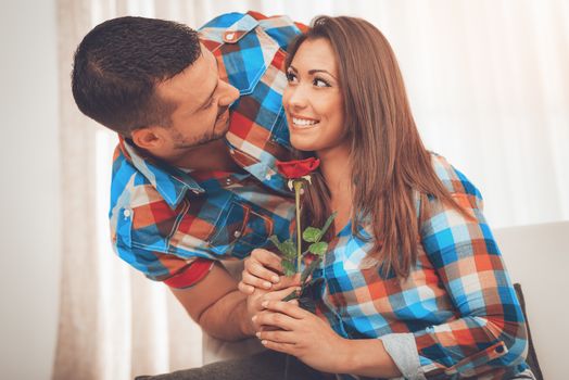 Handsome young man in love give red rose to his girlfriend in an apartment.