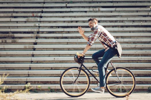 Casual handsome businessman going to work by bicycle. He is riding bike and waving Hello.