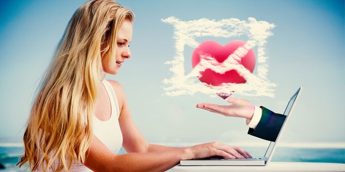 Composite image of pretty blonde using her laptop at the beach with hand presenting heart email