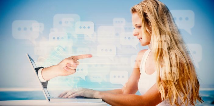 Composite image of pretty blonde using her laptop at the beach with hand pointing