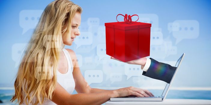 Composite image of pretty blonde using her laptop at the beach with hand presenting gift