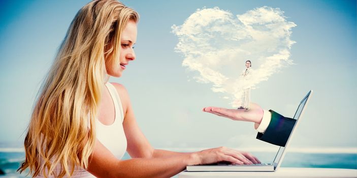 Composite image of pretty blonde using her laptop at the beach with heart cloud and hand