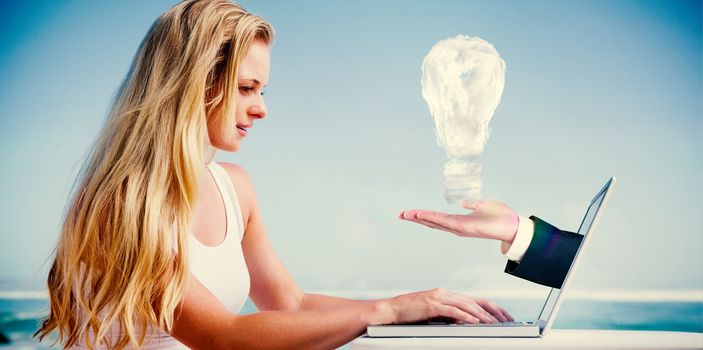 Composite image of pretty blonde using her laptop at the beach with hand presenting cloud bulb