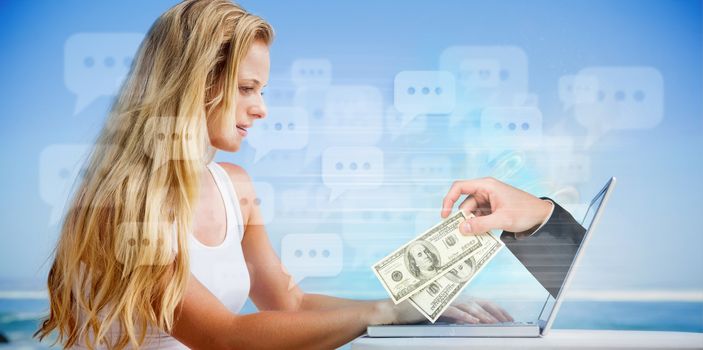 Composite image of pretty blonde using her laptop at the beach with hand holding money