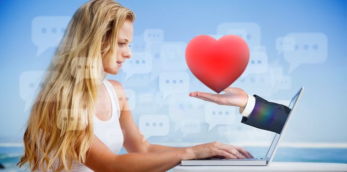 Composite image of pretty blonde using her laptop at the beach with hand holding heart