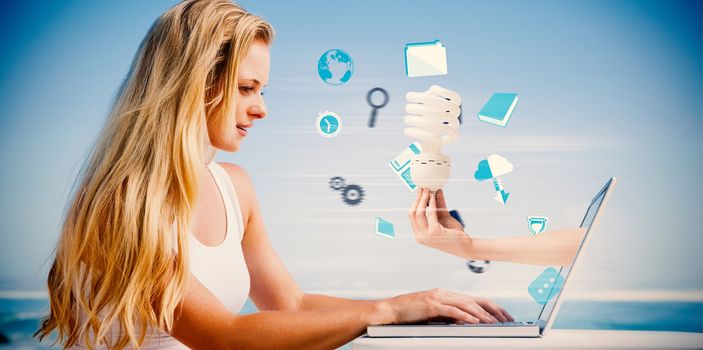 Composite image of pretty blonde using her laptop at the beach with hand holding bulb