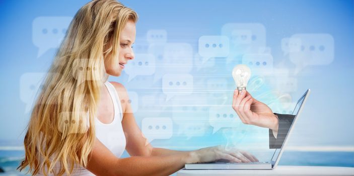 Composite image of pretty blonde using her laptop at the beach with hand holding bulb