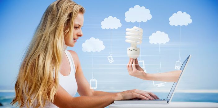 Composite image of pretty blonde using her laptop at the beach with hand holding bulb