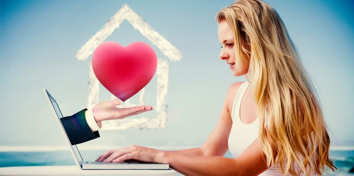 Composite image of pretty blonde using her laptop at the beach with hand presenting heart