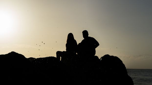 Couple's silhouette sitting on the rocks enjoying the sun