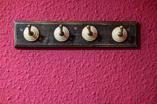 Four hook coat rack, vintage style, with wooden base on a magenta wall