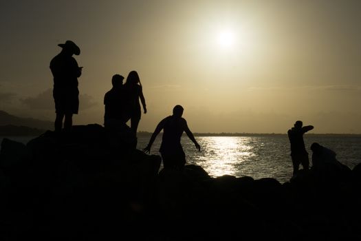Friends silhouette sitting on the rocks enjoying the sun
