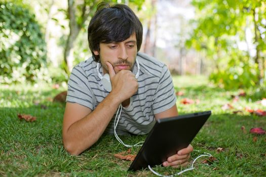 young man relaxing with a tablet pc listening music with headphones on a the park, outdoor