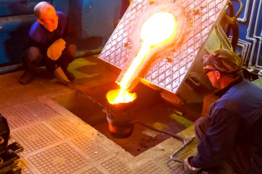 Saratov, Russia - November 23, 2017: Furnace for metal remelting. Pouring metal from the furnace by workers.