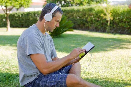 young man relaxing with a tablet pc listening music with headphones on a the park, outdoor