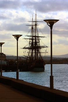 Vertical shot of an old sailing ship moored at a pier with cloudy sky background