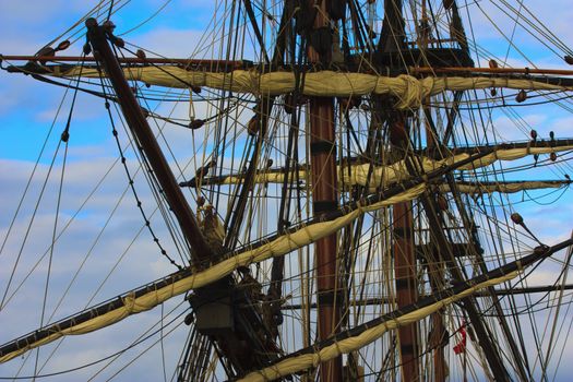 Masts and spars and furled sails of an old sailing ship with the sky in the background