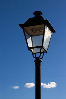 A vertical shot of an ornate street light with the sky and a lone cloud in the background