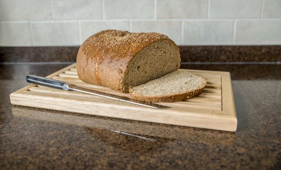 freshly baked bread with a cut slice with a kitchen knife on a wooden plant in the kitchen