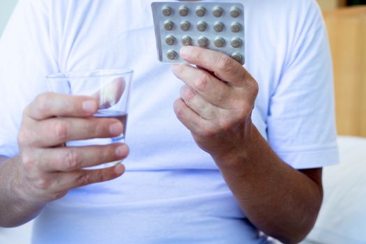 Cropped image of Sick man holding blister pack with tablets and glass of water at home. Treatment. Pharmaceutical drug. Medicine and medication.   