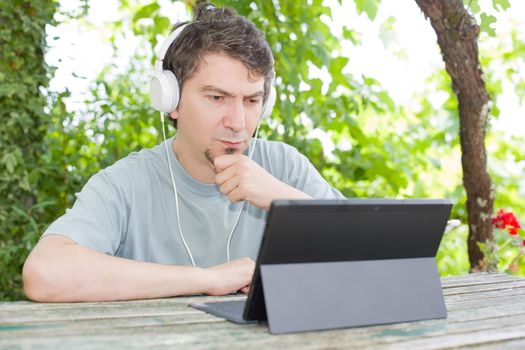 young man relaxing with a tablet pc listening music with headphones on a the park, outdoor