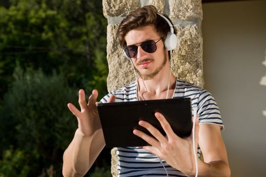 young man relaxing with a tablet pc listening music with headphones, outdoor