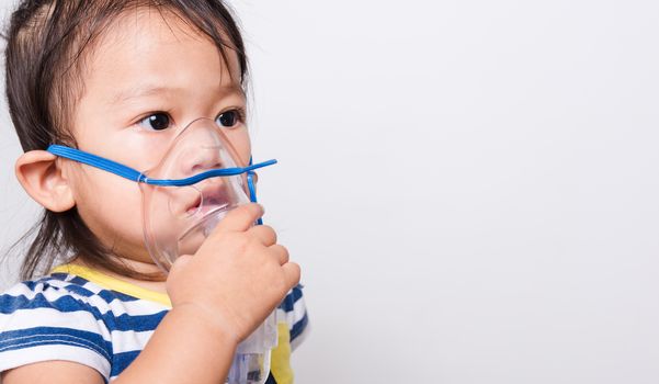 Closeup Asian face, Little baby girl sick her using steam inhaler nebulizer mask inhalation oneself on white background with copy space, health medical care