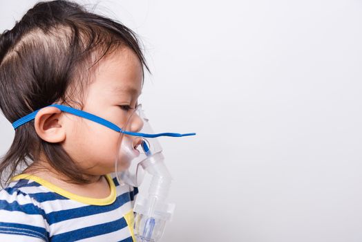 Closeup Asian face, Little baby girl sick her using steam inhaler nebulizer mask inhalation oneself on white background with copy space, health medical care