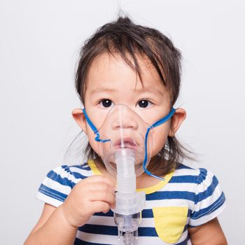 Closeup Asian face, Little baby girl sick her using steam inhaler nebulizer mask inhalation oneself on white background with copy space, health medical care