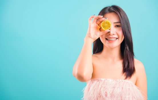 Portrait asian beautiful woman smiling her holding halves of orange on face near eyes on blue background, with copy space for text