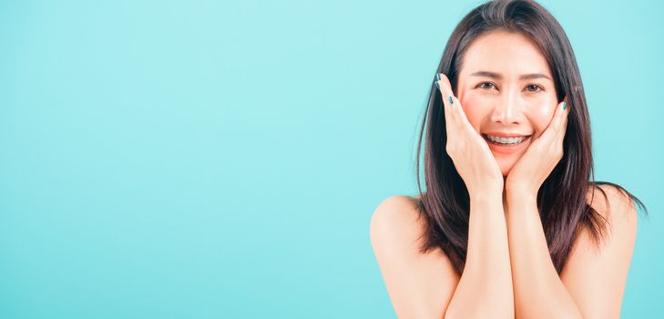 Smiling face Asian beautiful woman her hands touch on face skin on blue background, with copy space for text