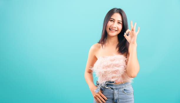 Portrait asian beautiful woman smiling showing hand okay sign her looking to camera on blue background, with copy space for text