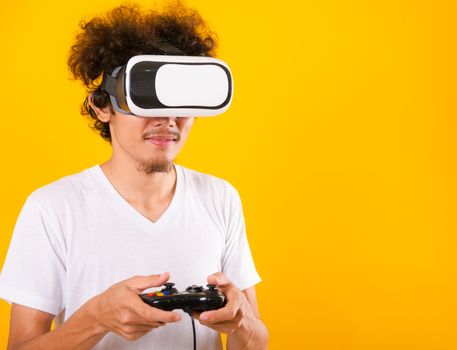 Asian handsome man with curly hair play game he using virtual reality headset or VR glass isolate on yellow background with copy space for text