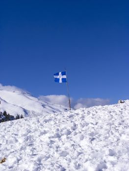 Greek flag at Ziria mountain covered with snow on a winter day, Korinthia, South Peloponnese, Greece. Ziria is one of the snowiest mountains in Peloponnese (2,374m).