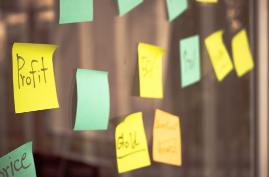 Colleagues wrote the organization's goals on paper notes on a glass board by brainstorming. This image focus on profit message and color in vintage style.