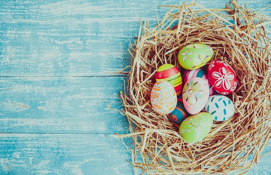 Easter eggs in various patterns and colors in a bird's nest placed on a wooden floor decorated in retro style.