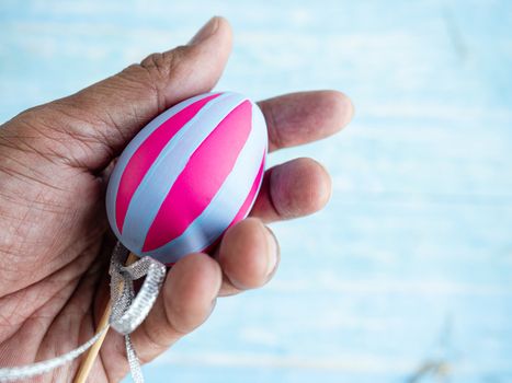 A man's hand is extending the pink and white stripes of the Easter egg that has already been adorned and decorated.