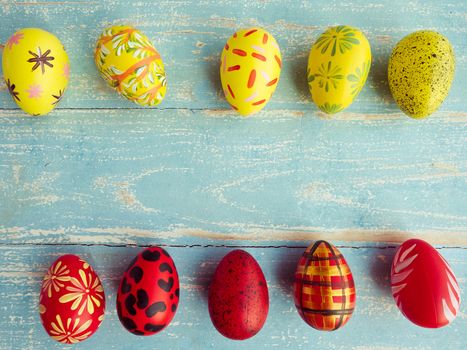 Easter eggs are arranged in two rows between yellow and red on a pastel blue wood floor. Vintage style coloring