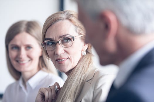 Business people sitting in a row and working in office, focus on mature woman in glasses