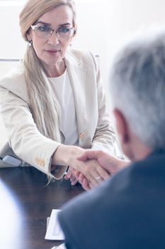 Business people shaking hands at meeting table focus at mature woman