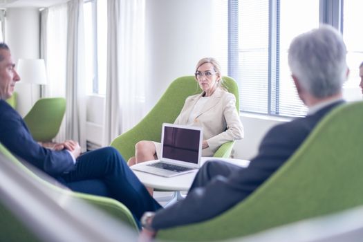 Business people sitting together on armchairs in office hall and having a negotiation discussion