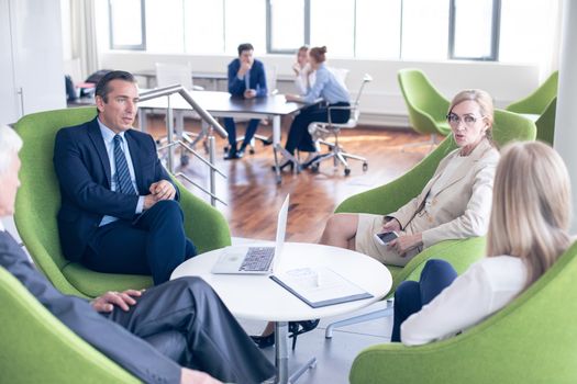 Business people sitting together on armchairs in office hall and having a negotiation discussion