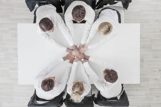 Business people team stacking hands sitting around white conference table in office unity cooperation concept