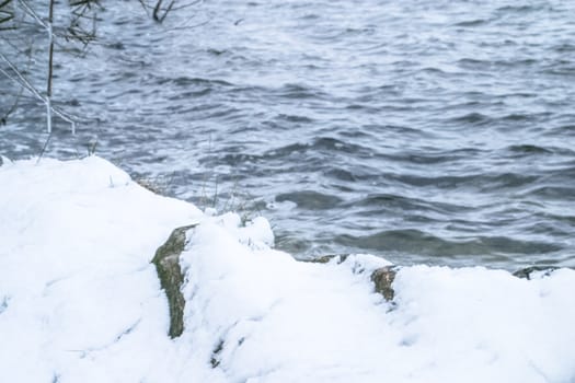 Cliff Shore of the river with waves and ruffles water in a winter frosty weather. River shore with snow in winter