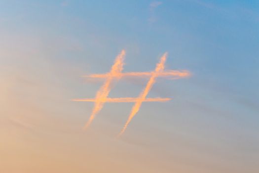 Hashtag sign in sky at sunset, icon made out of contrail clouds. Social media and microblogging concept.