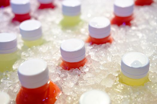 Close-up of Fresh juice of different exotic fruits bottles on the ice box. Mix of plastic bottles on the ice bucket for sale in food market. 