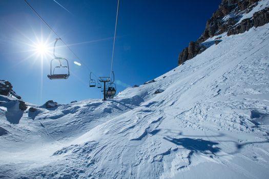 Ski lift chairs on bright winter day Dolomities Dolomiti Italy in wintertime beautiful alps mountains and ski slope Cortina d'Ampezzo Cinque torri mountain peaks famous landscape skiing resort area