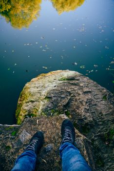 Men's legs stand on a stone in front of the lake. Flooded stones in the water.