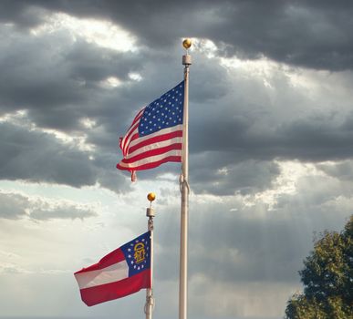 United States and Georgia Flags on poles against blue sky